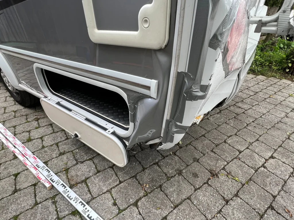 Beschädigte vordere Aufbauecke eines Wohnmobils mit angelegtem Maßband