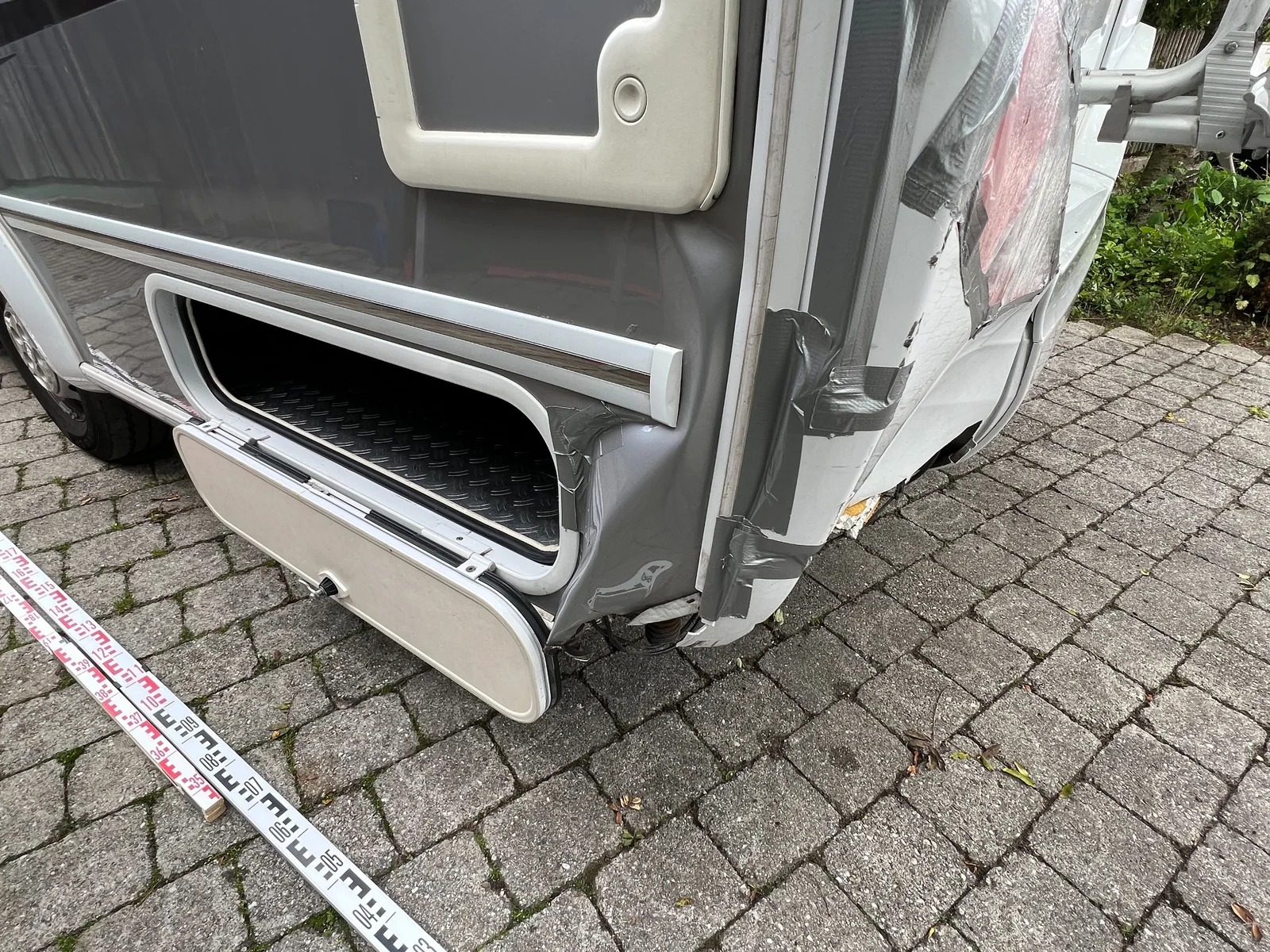 Beschädigte vordere Aufbauecke eines Wohnmobils mit angelegtem Maßband